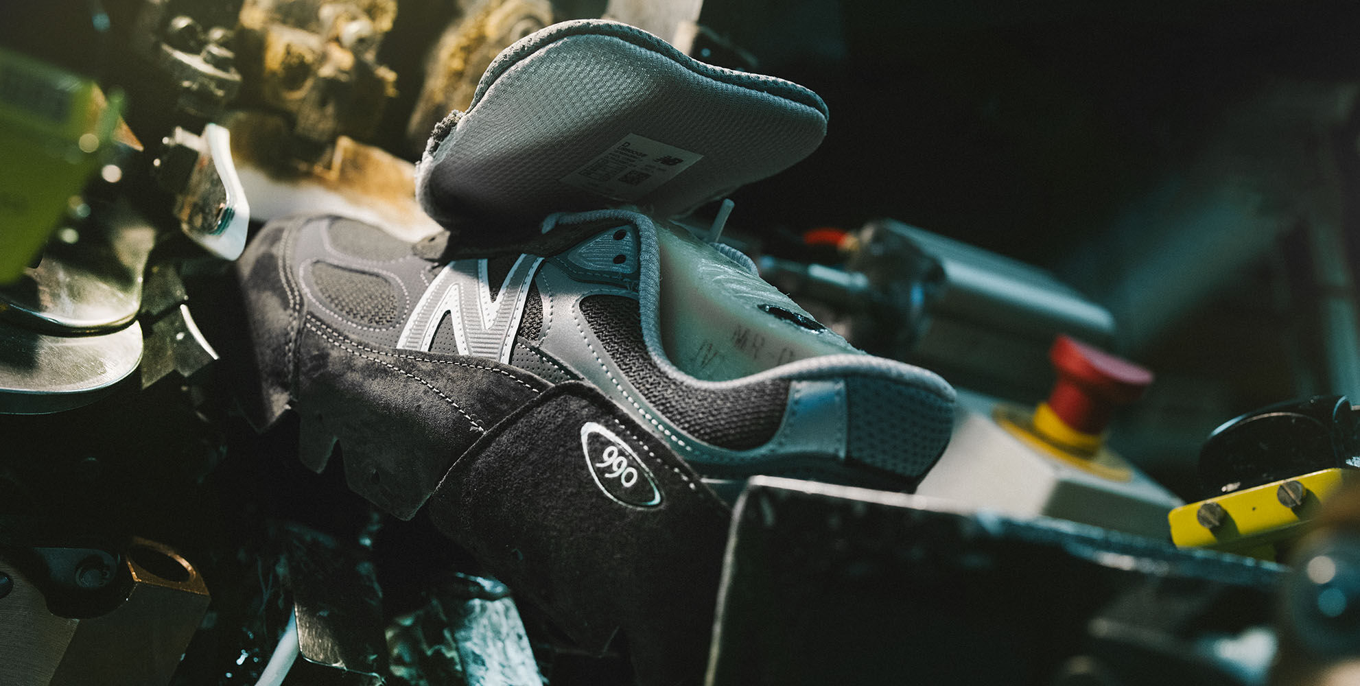 A New Balance sneaker sitting in equipment and being constructed in a factory setting.